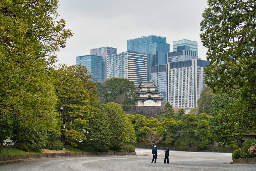 Bild vom Kaiserpalast in Tokio, einer der Top Sehenswürdigkeiten in Tokyo. Im Vordergrund ist der ruhige Garten zu sehen und ein Yagura und im Hintergrund Bürogebäude.